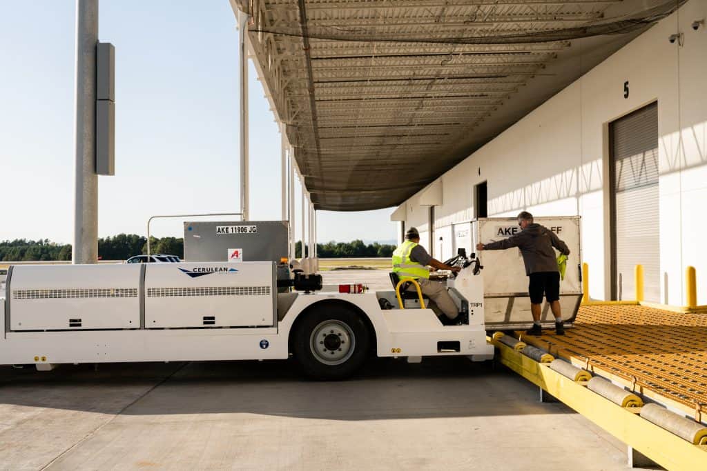 Man loading cargo containers onto a tug at Cerulean Aviation